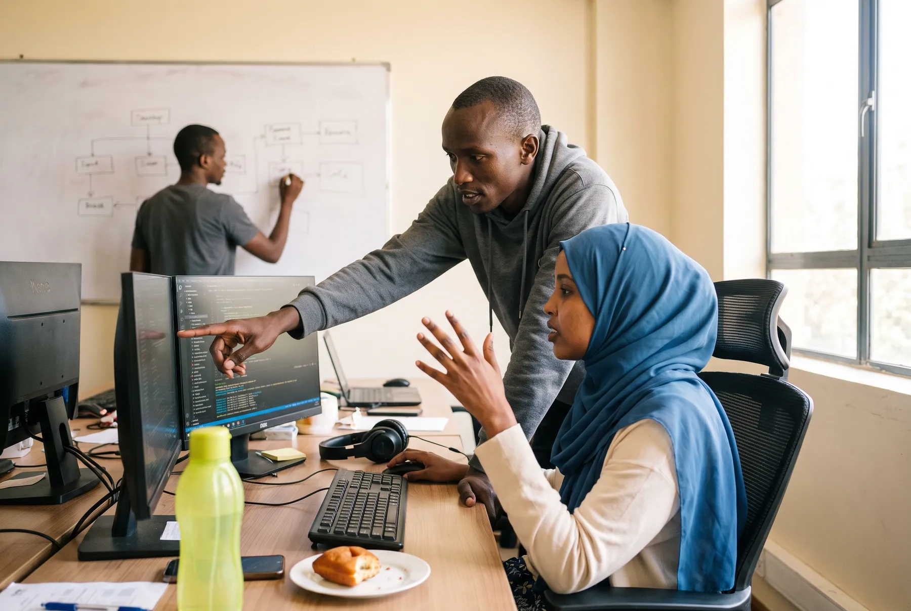 Two Kenyan engineers talk through code at a desk in a Nairobi office